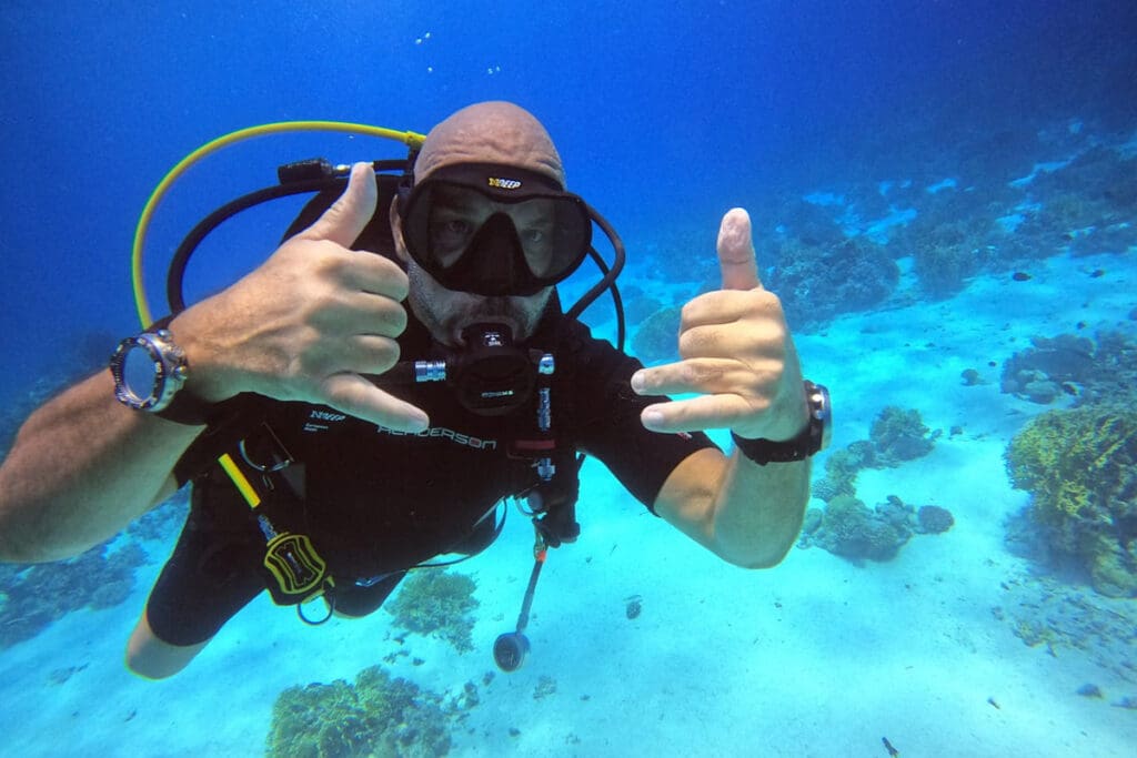 A man in black wetsuit holding up two thumbs.
